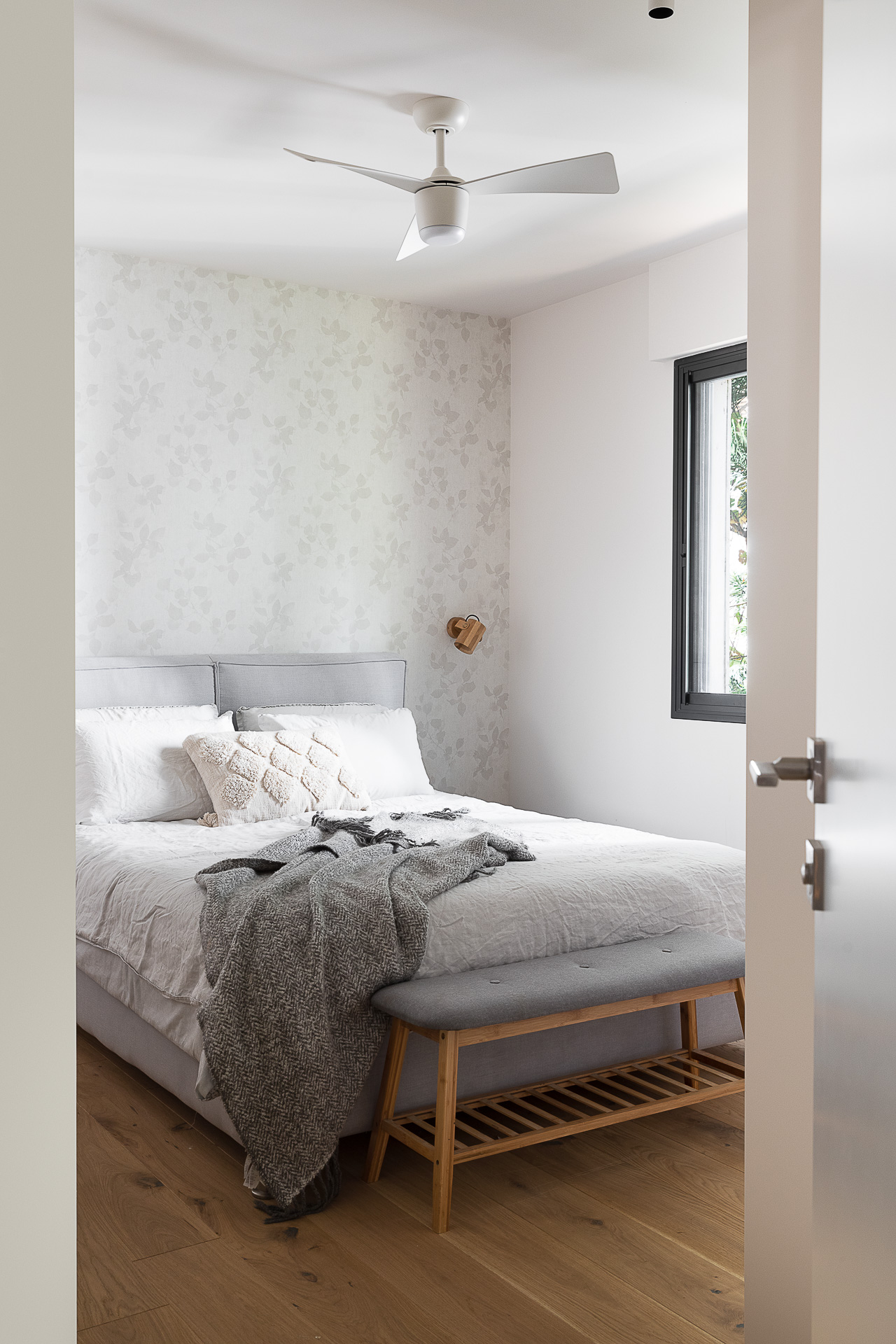 A calm bedroom with softly patterned wallpaper and natural timber